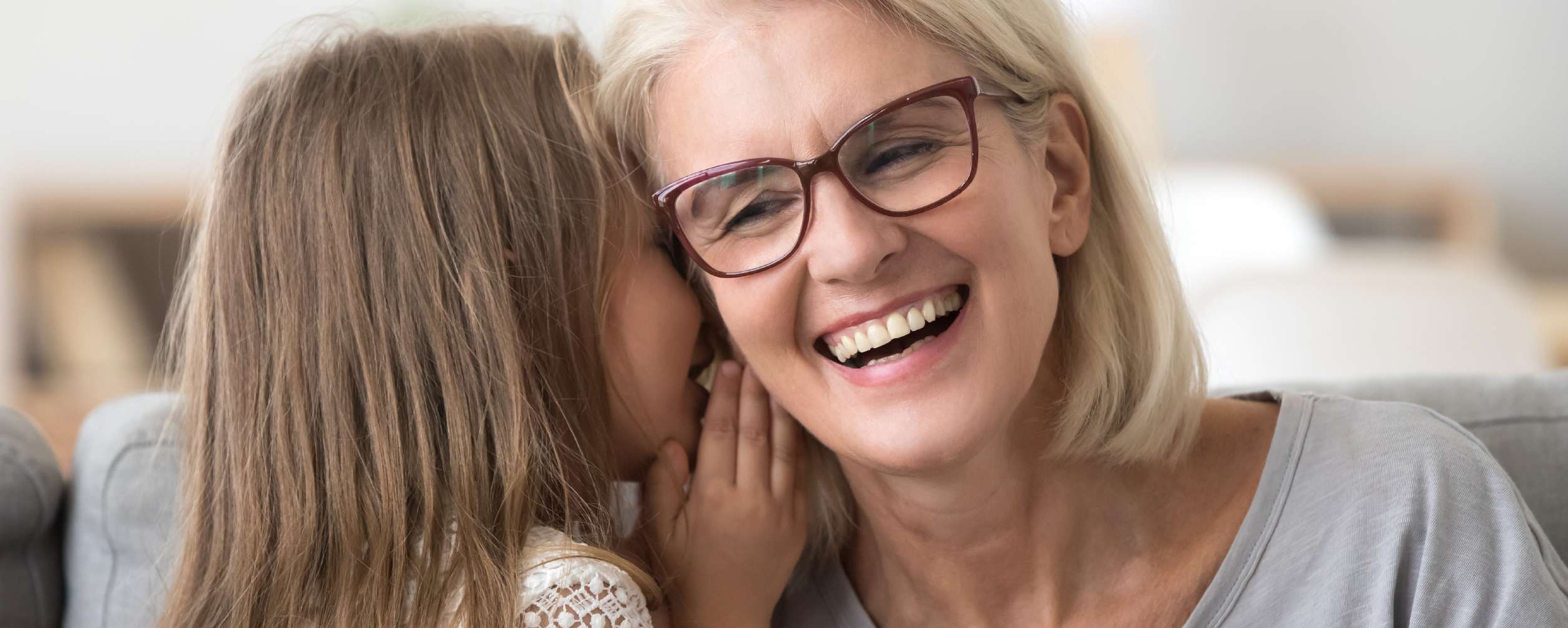 Kleines Mädchen flüstert glücklicher Frau etwas zu.