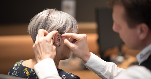 Hörakustiker passt einer Kundin ein Hörgerät an